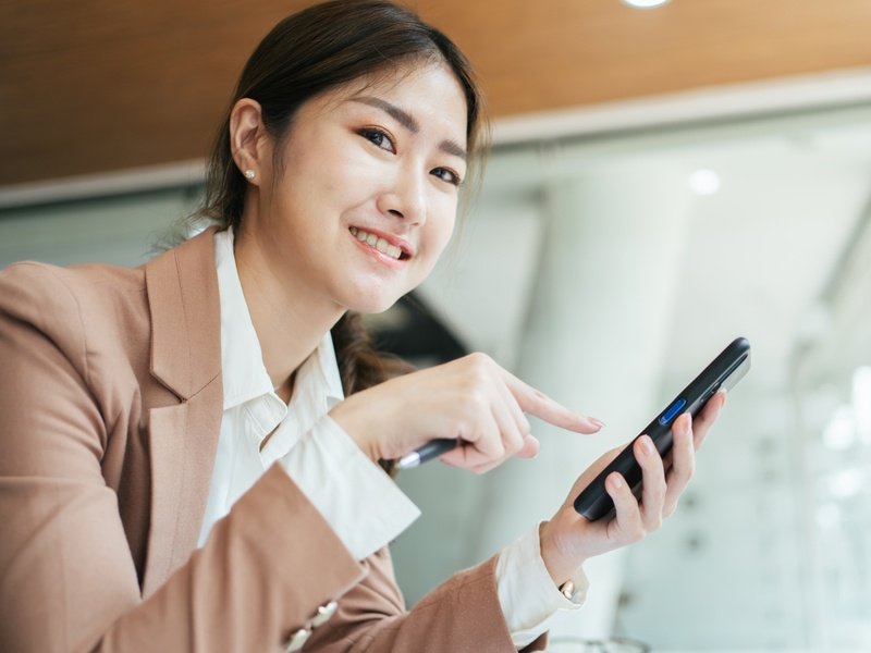 オフィスでスマートフォンとノートパソコンを使用しているアジア女性。