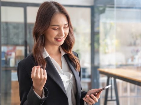 マーケティング、財務、会計、企画、アジアの女性起業家がスマートフォンを手にビジネス経営から利益を得ることに成功したという喜びを表す。