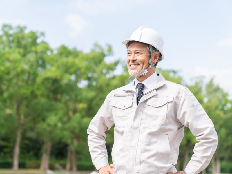 森を背景に風景を仰いでいる現場服姿の男性
