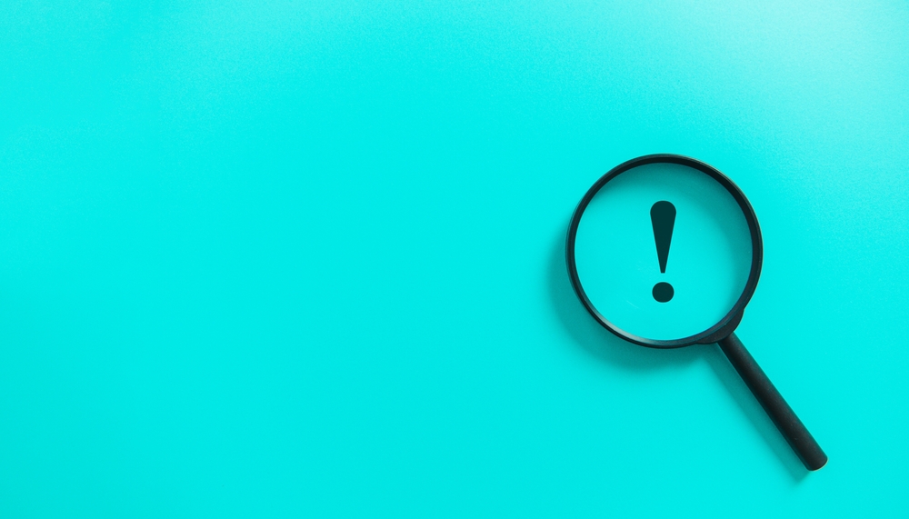 青い背景に感嘆符が描かれており、虫眼鏡で覗いている様子